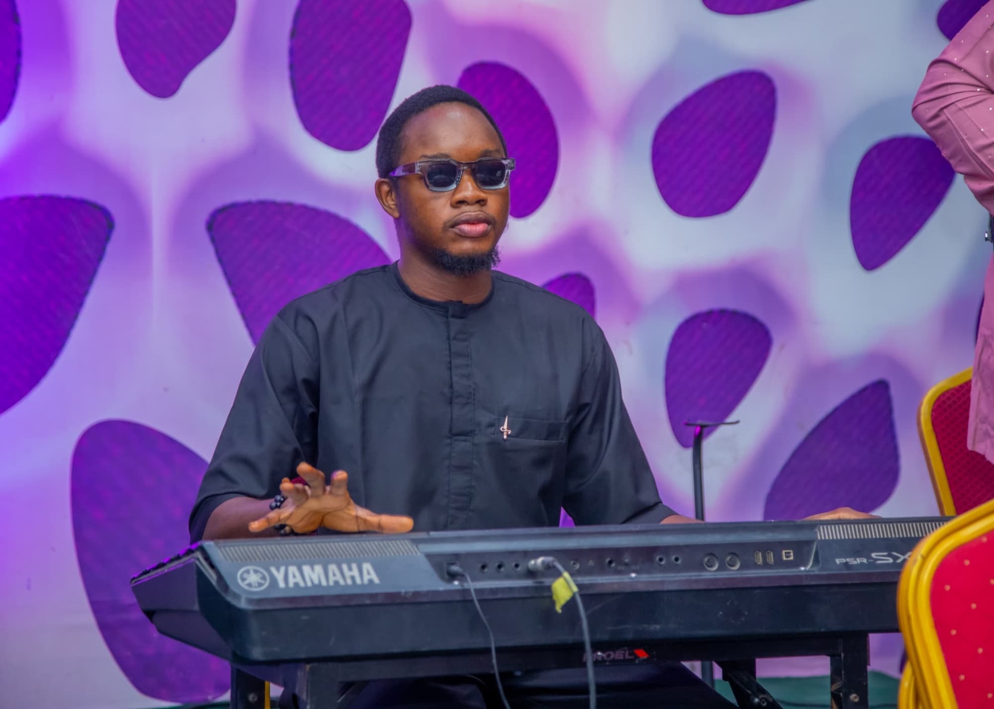 Oladimeji at a Yamaha keyboard in front of a violet patterned backdrop