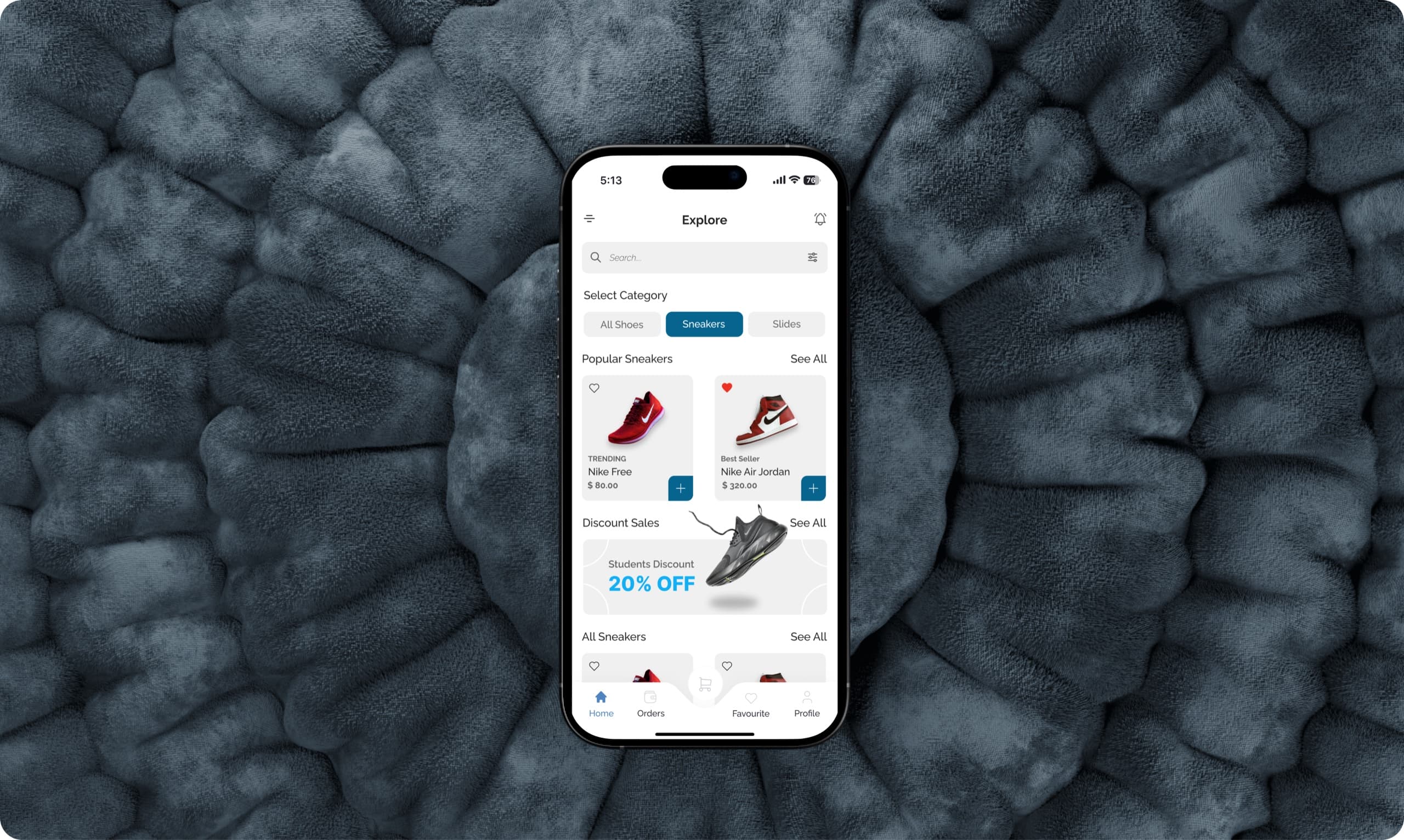 SneakerShop's Explore screen on an iPhone, lying on a slate-blue textured fabric